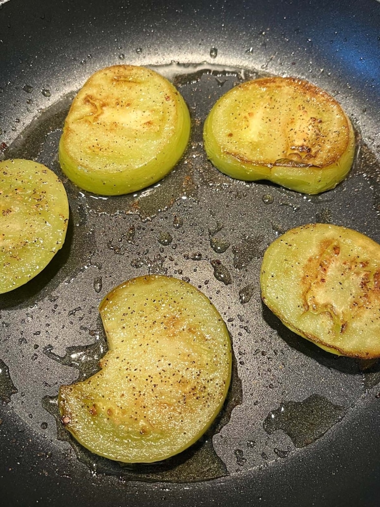 slices of green tomato frying in a skillet