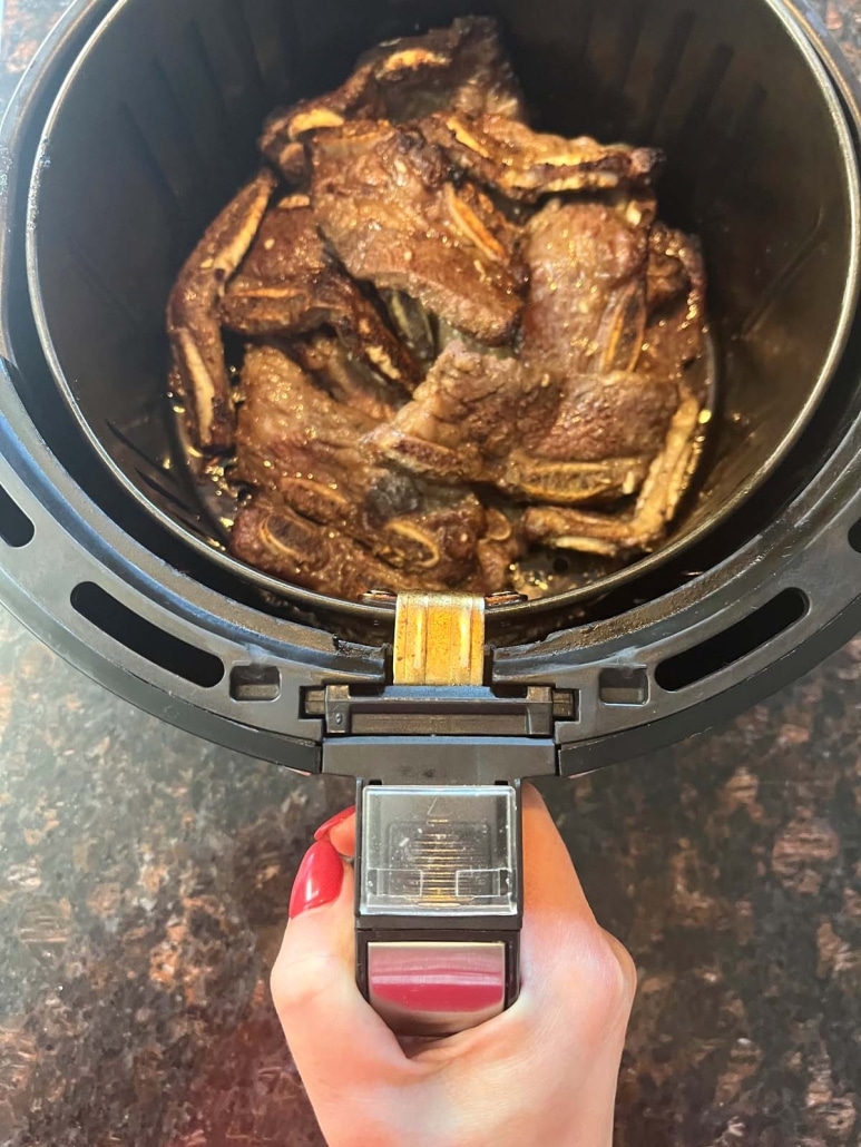 hand holding air fryer basket with short ribs inside