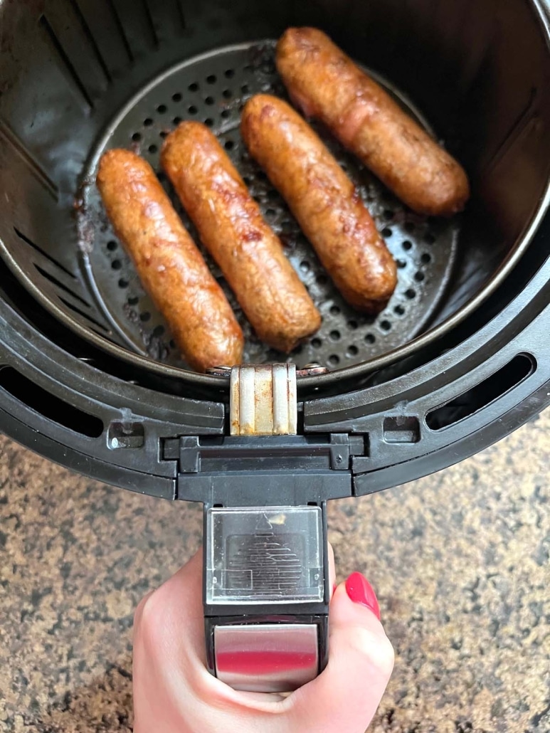hand holding air fryer basket with cooked meatless sausages