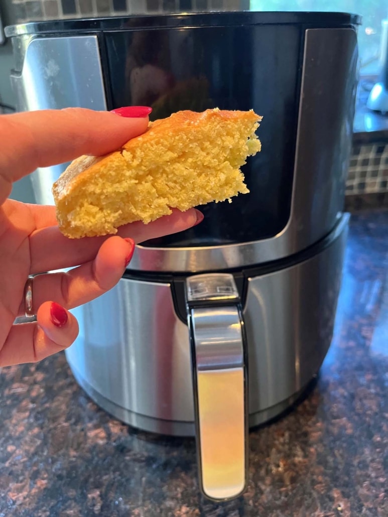 hand holding slice of cornbread in front of air fryer