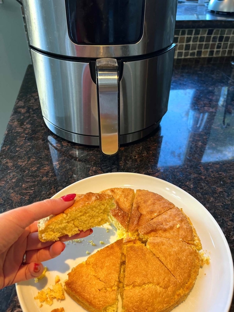 hand holding slice of Air Fryer Cornbread in front of air fryer appliance