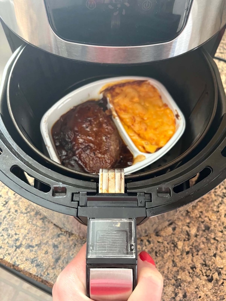 hand opening air fryer to show Salisbury steak dinner inside