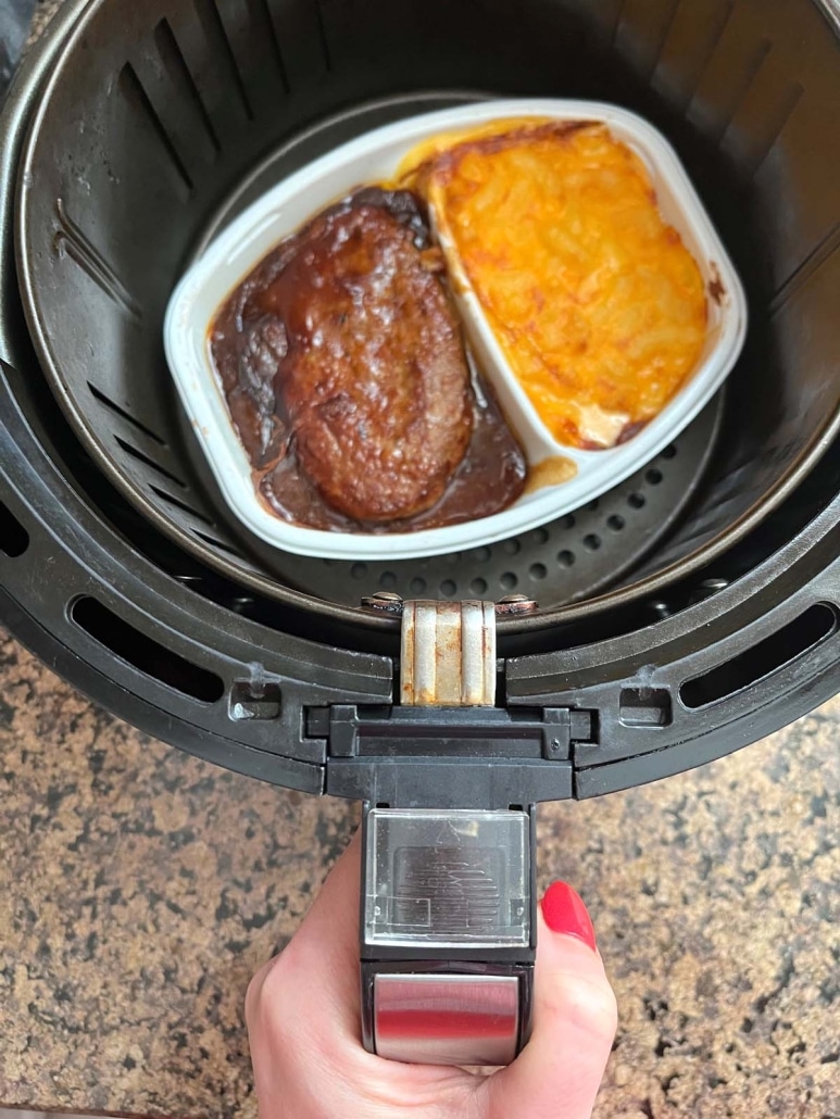hand holding an air fryer basket with convenient dinner Salisbury steak inside