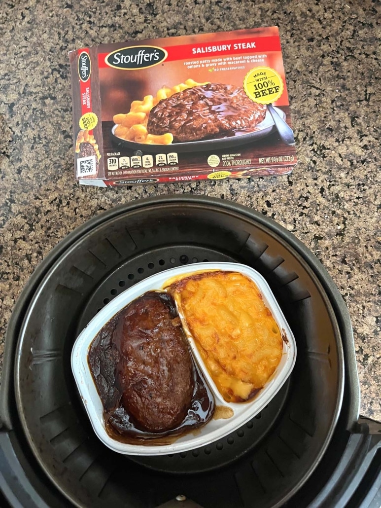 Salisbury steak dinner in an air fryer basket next to a package of frozen Salisbury steak