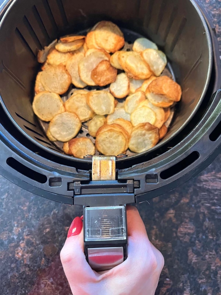hand holding air fryer basket with sliced potatoes inside