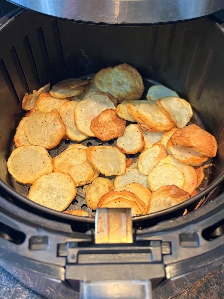 air fryer opened to show light and crispy potato slices inside