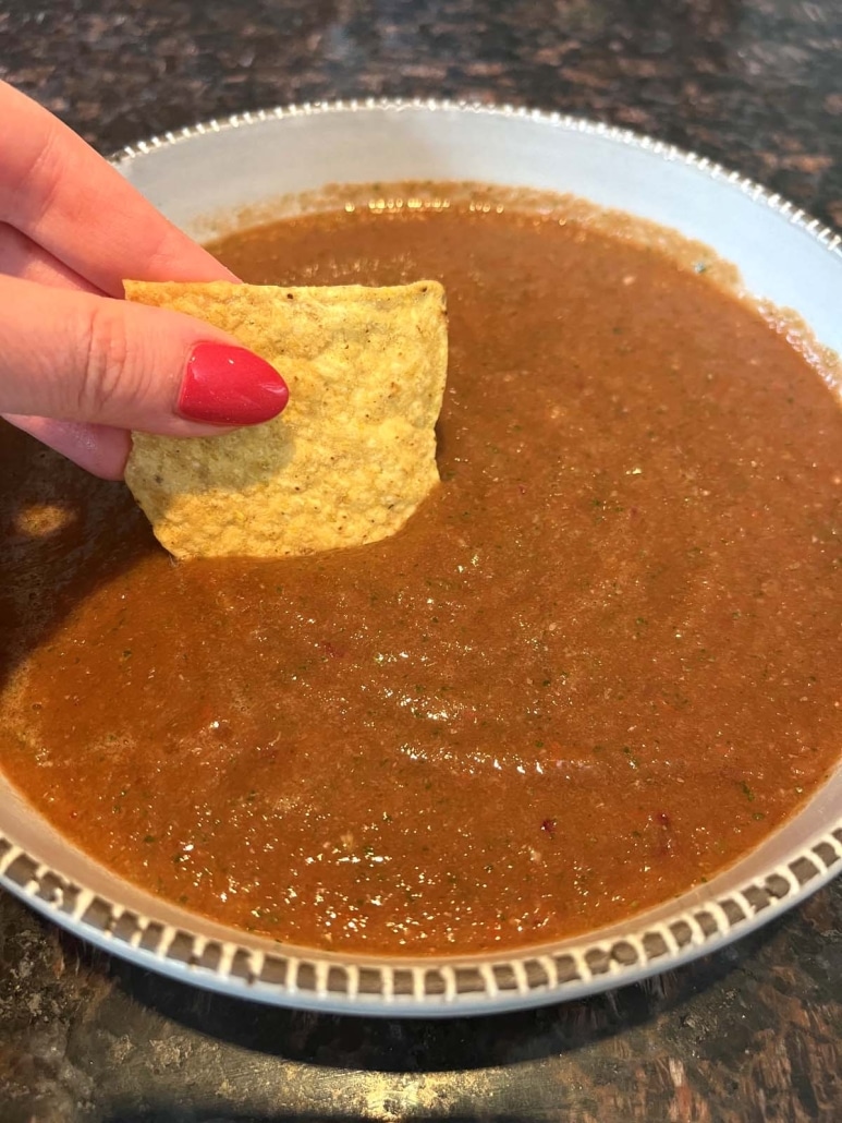 hand dipping a tortilla chip into fresh blender salsa