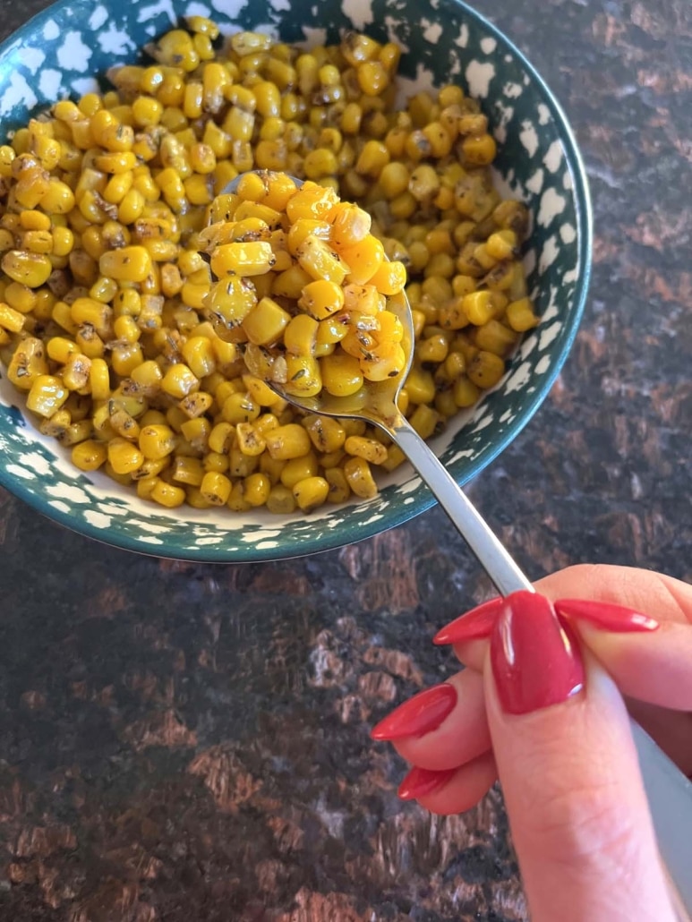 hand scooping out cooked corn from bowl