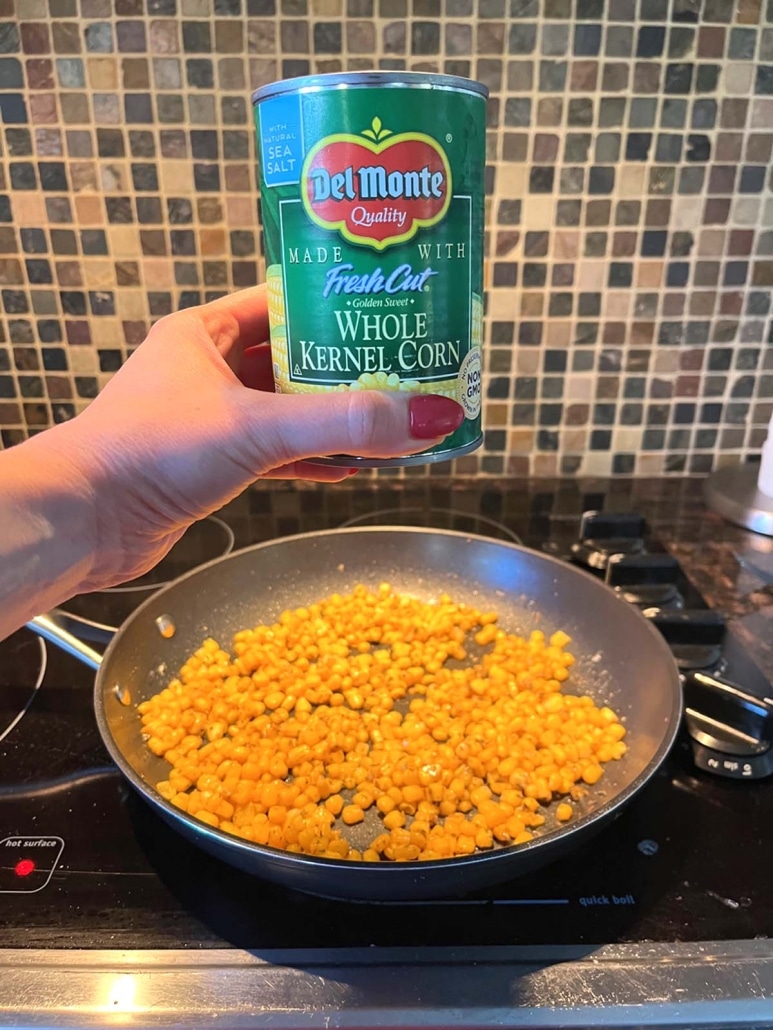 hand holding can of corn over cooked corn