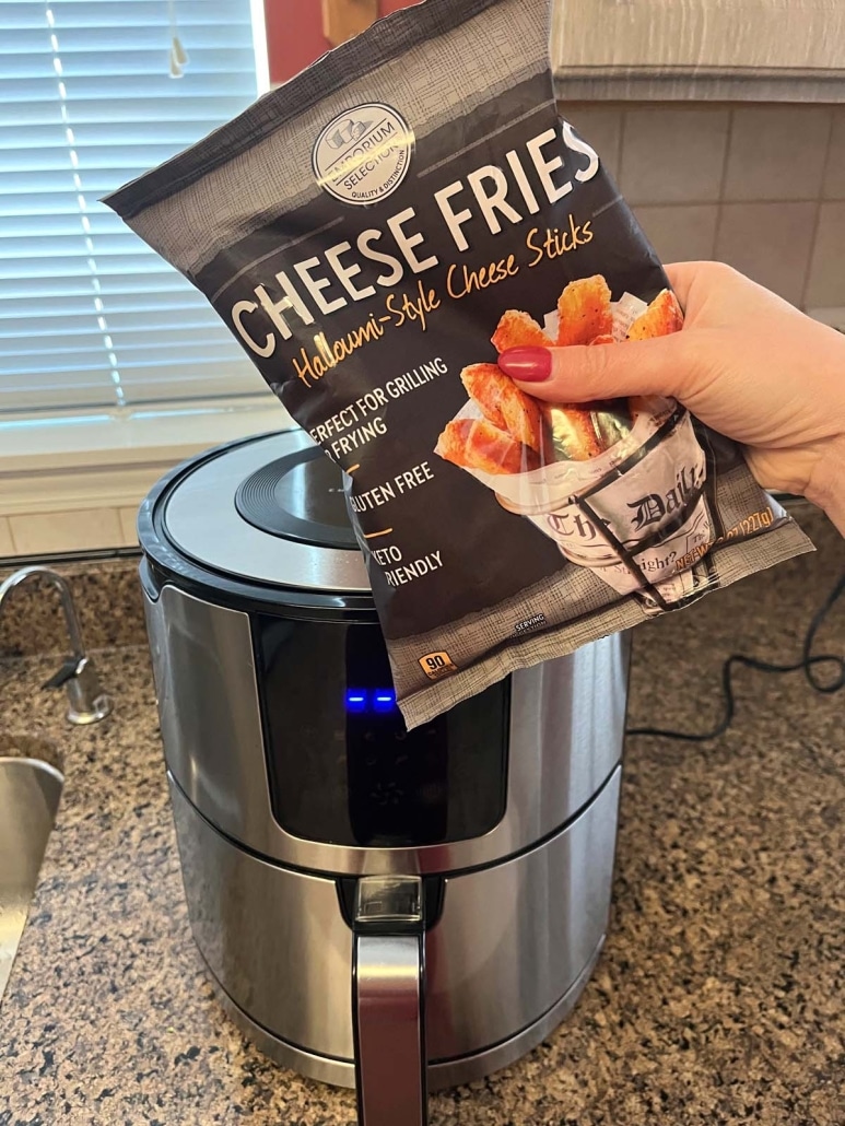 hand holding frozen package of Aldi Cheese Fries in front of an Air Fryer