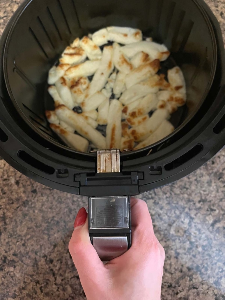 hand holding air fryer basket containing roasted cheese fries
