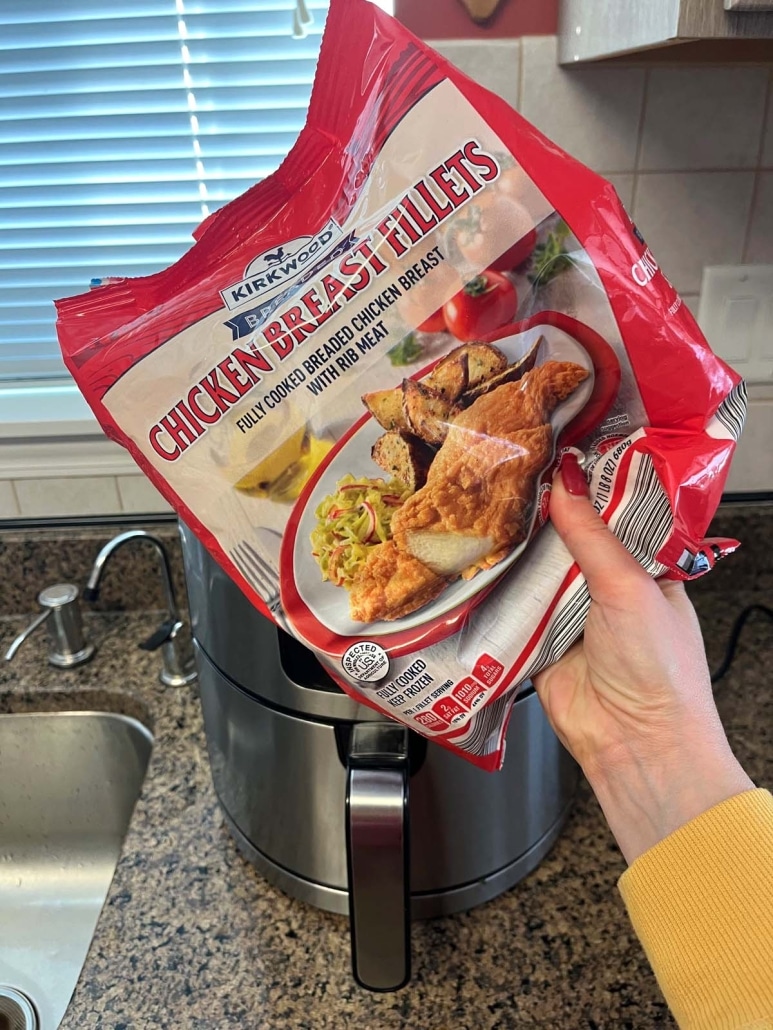 hand holding package of popular frozen item Aldi red bag chicken in front of an air fryer