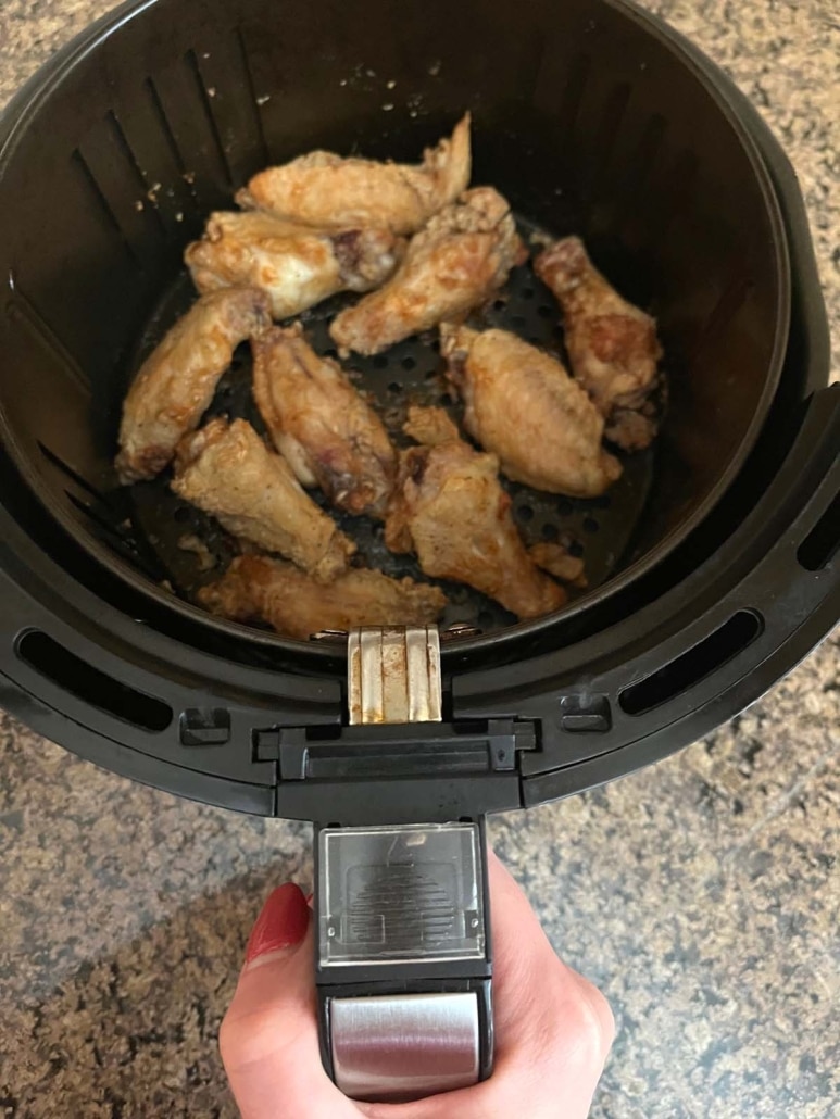 hand holding air fryer basket with crispy chicken wings inside
