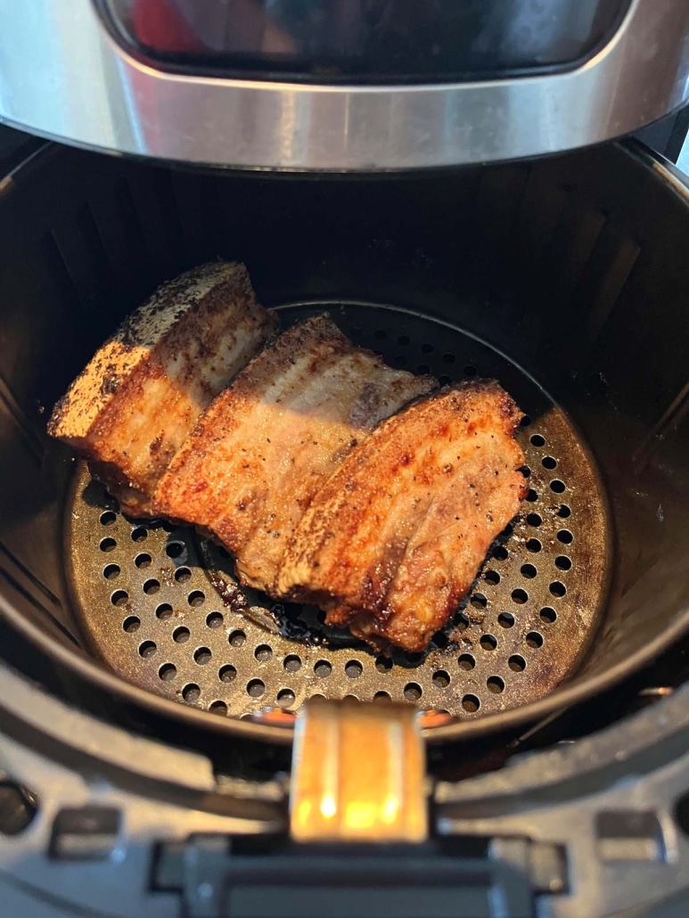 air fryer opened to show tasty pork belly slices cooking inside