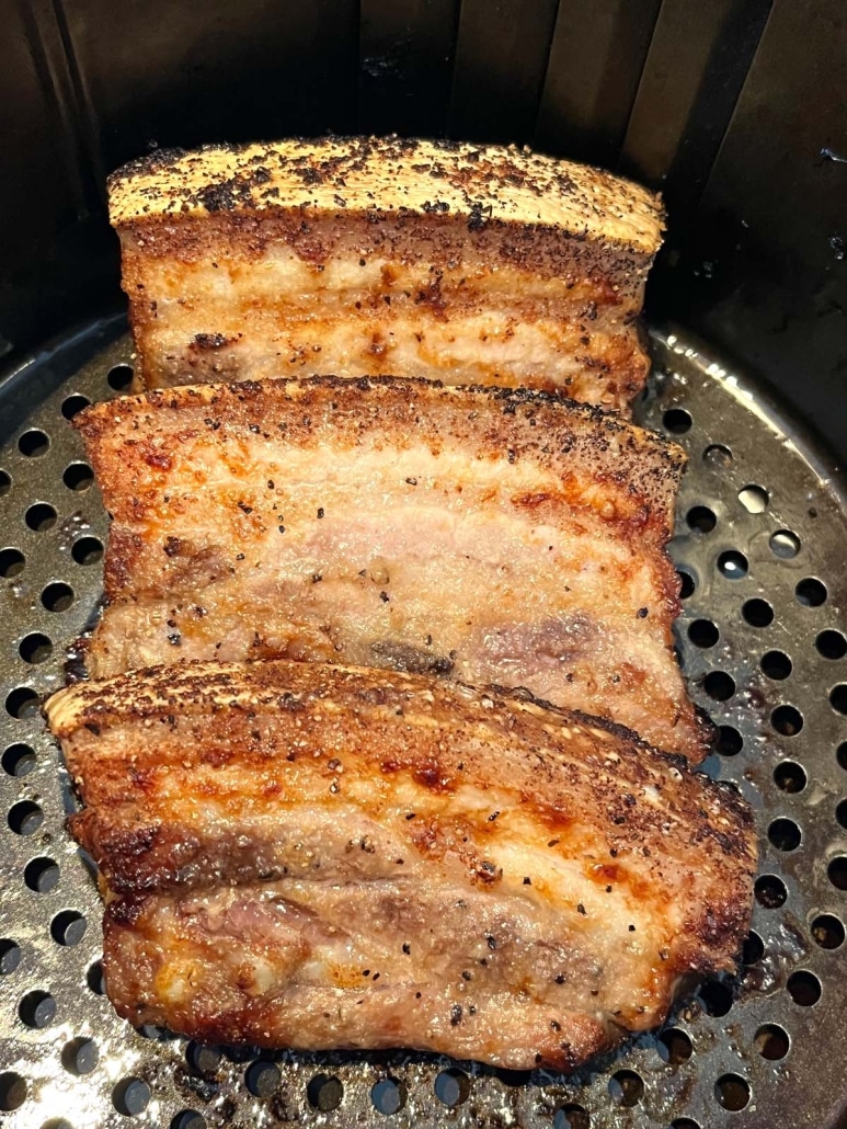 pork belly slices cooking in an air fryer basket