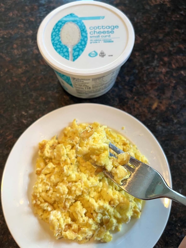 plate of cottage cheese scrambled eggs with a fork, next to a container of cottage cheese