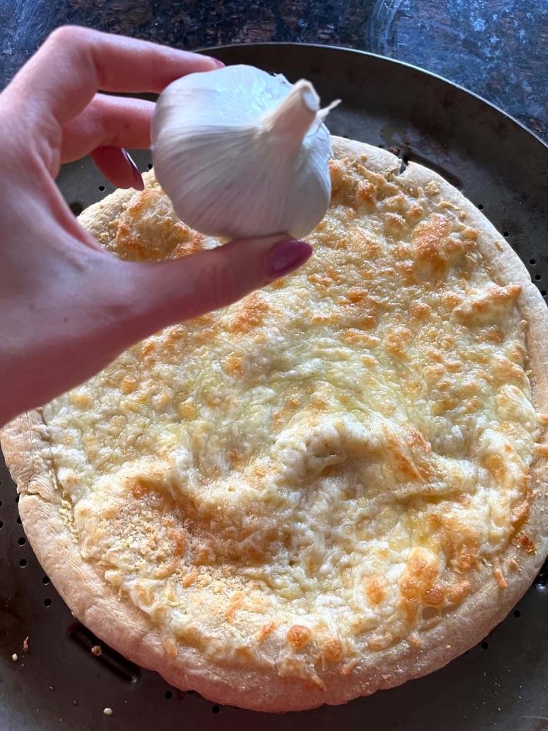 hand holding a bulb of garlic over a freshly baked Garlic Pizza