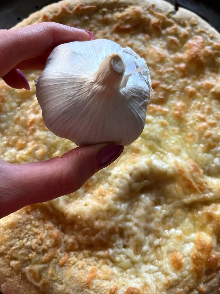 hand holding bulb of garlic in front of Garlic Pizza