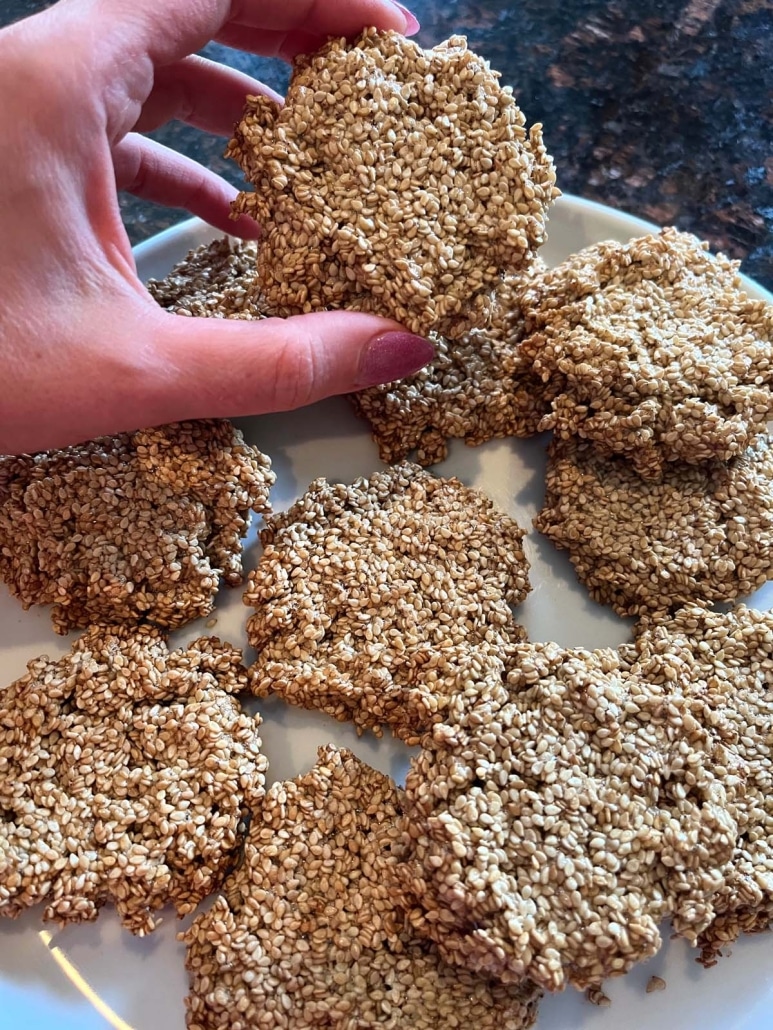 hand holding golden and crisp Sesame Cookie, in front of a plate of cookies