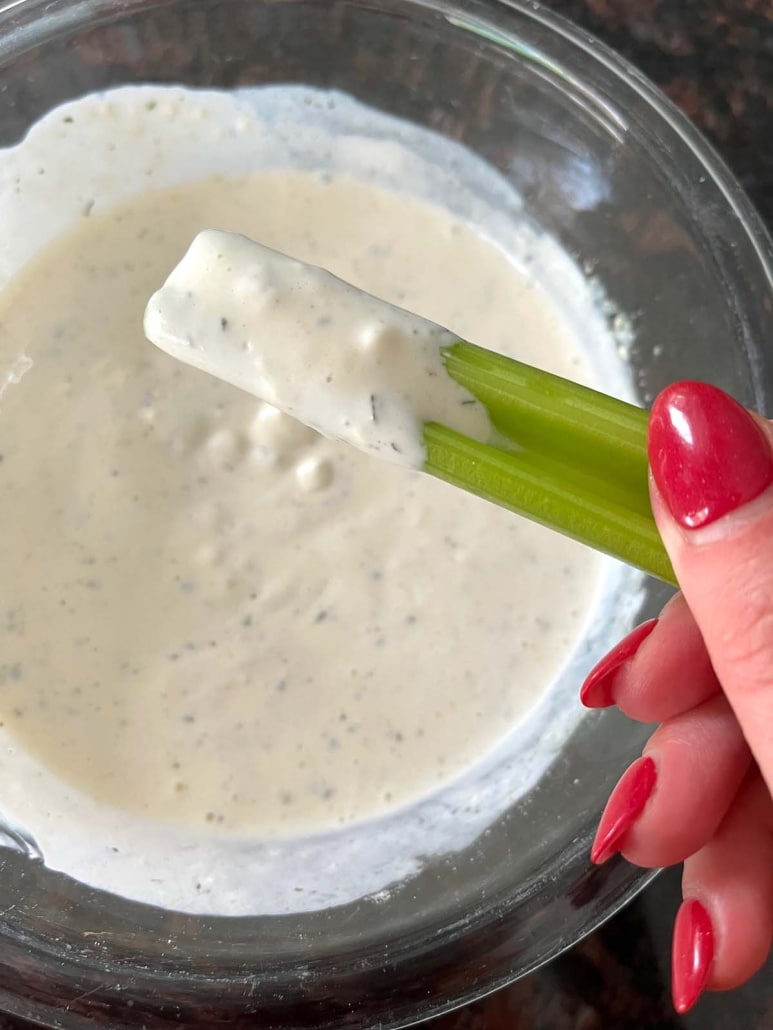 hand holding celery stick with homemade ranch dressing