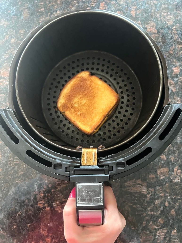 hand holding air fryer basket with grilled ham and cheese inside