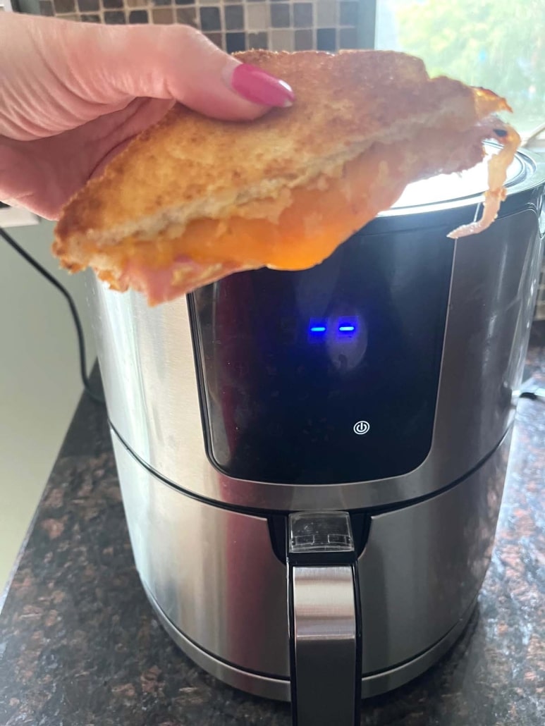 hand holding grilled ham and cheese sandwich in front of the air fryer