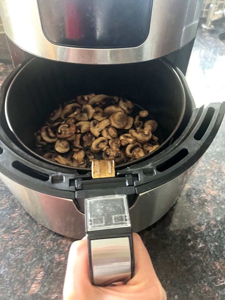 air fryer opened to show sliced mushrooms cooking inside
