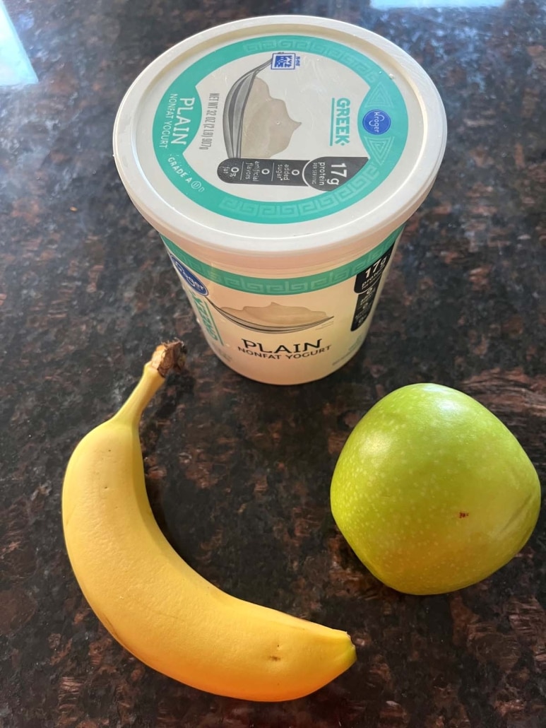 a container of Greek yogurt next to a banana and an apple