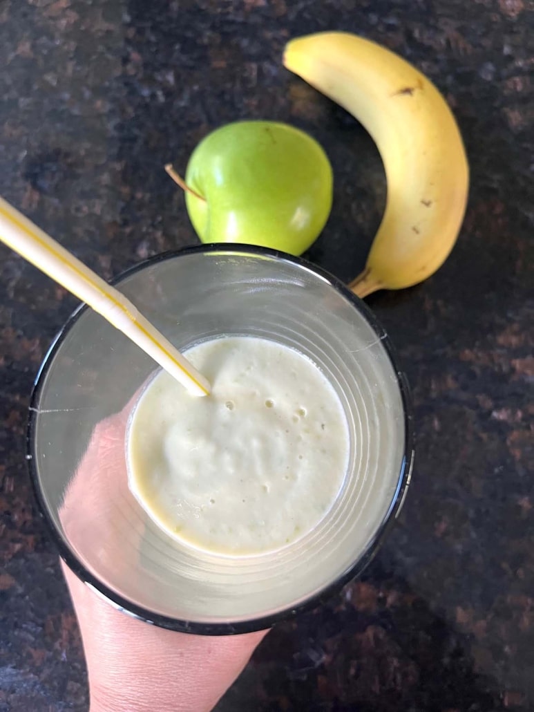 hand holding Apple Banana Smoothie next to an apple and a banana