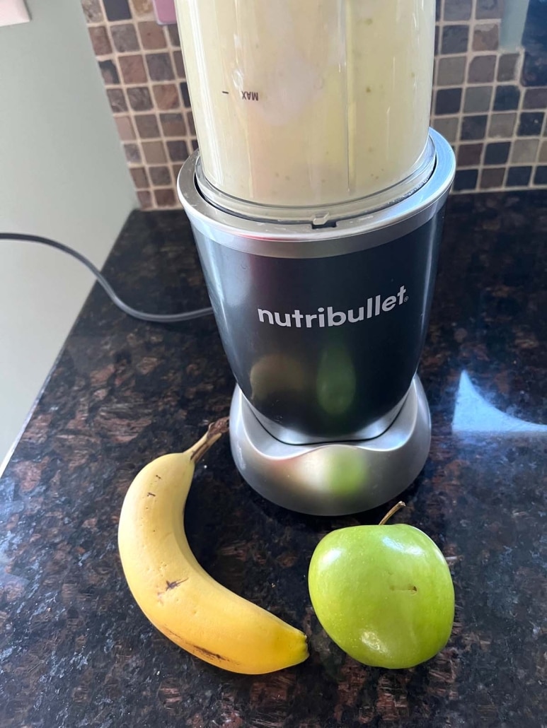 blender full of Apple Banana Smoothie, next to an apple and a banana