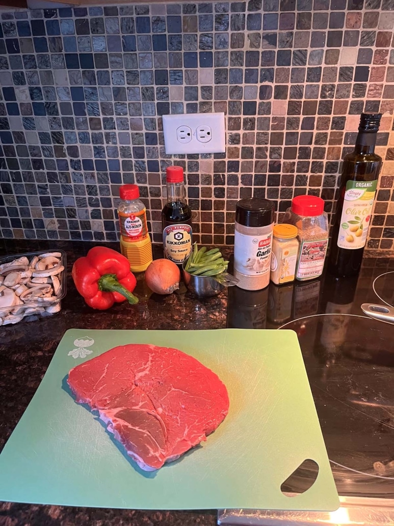angus sirloin steak on a cutting board next to vegetables and ingredients for sauce