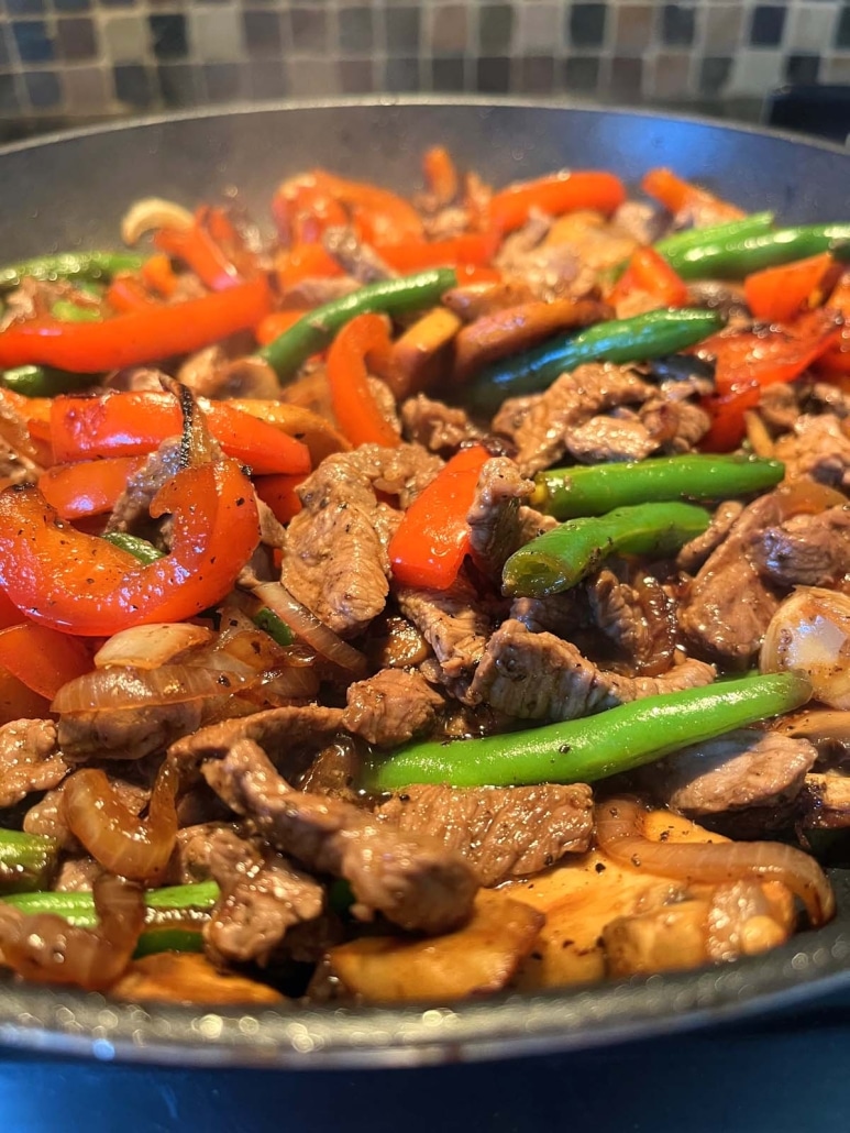 black pepper angus steak and vegetables sautéing in a hot skillet 