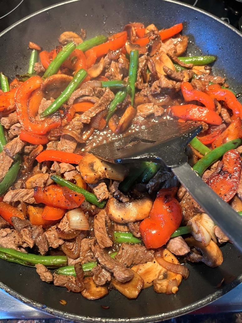 cooking black pepper angus steak and vegetables in a skillet