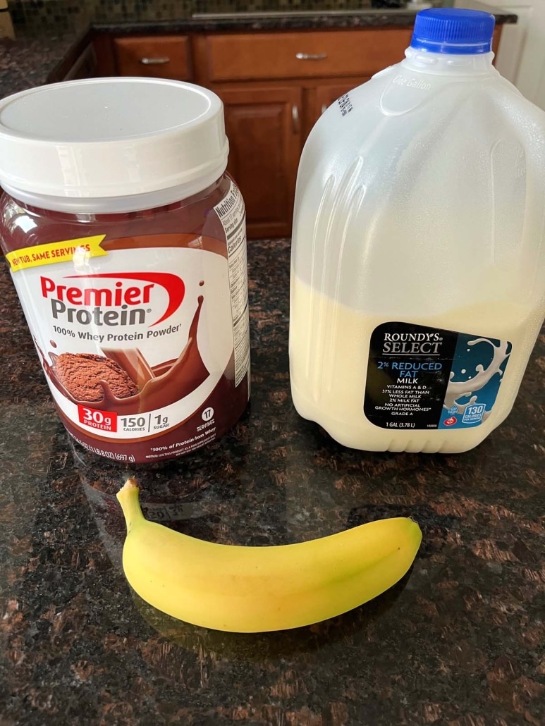 a gallon of milk, chocolate protein powder, and a banana on a countertop