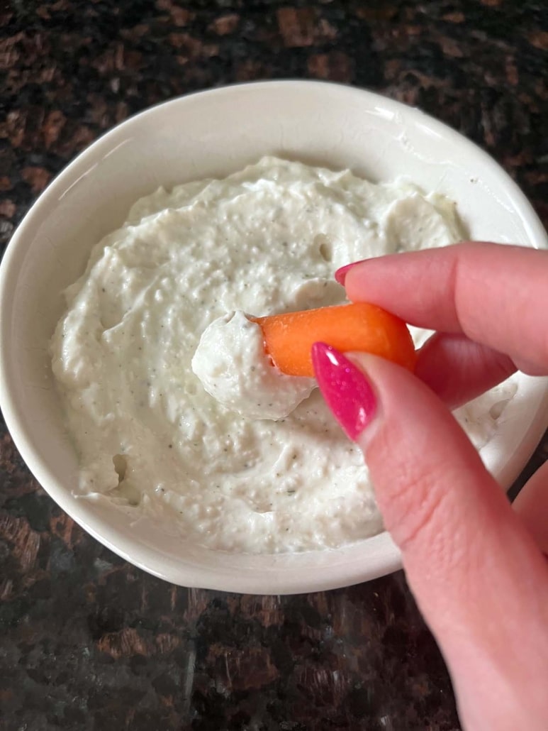 hand scooping up Cottage Cheese Ranch Dip with a carrot
