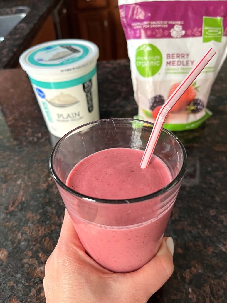 Mixed Berry Smoothie in a glass in front of a container of yogurt and a bag of frozen mixed berries