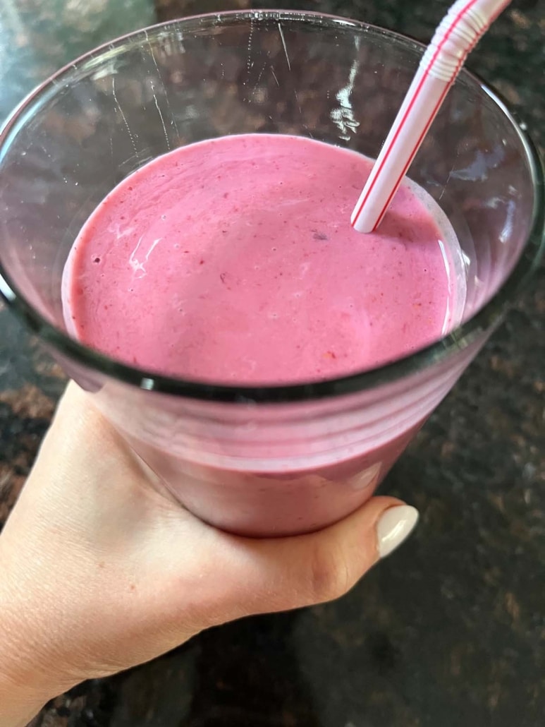 hand holding a Mixed Berry Smoothie with a straw in it