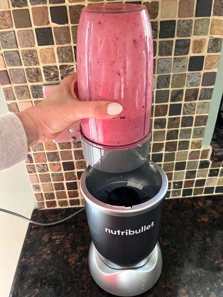 hand holding blender cup with Mixed Berry Smoothie inside