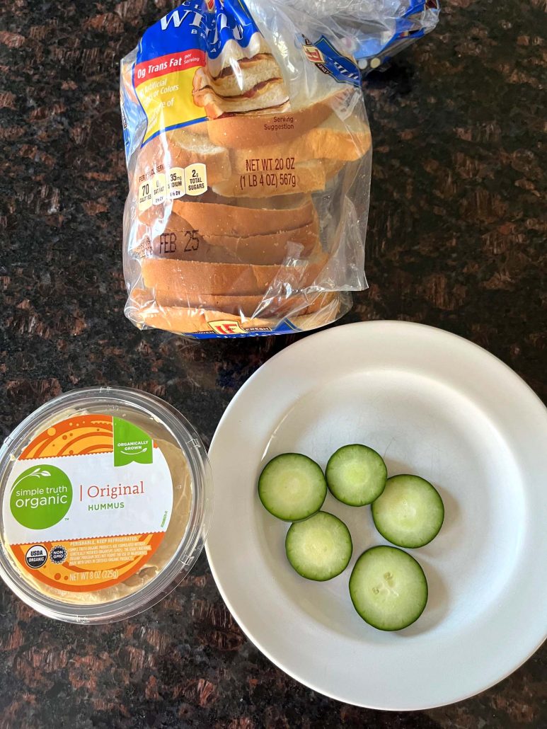 ingredients for Hummus Toast: a bowl of sliced cucumbers, a container of hummus, and a bag of bread