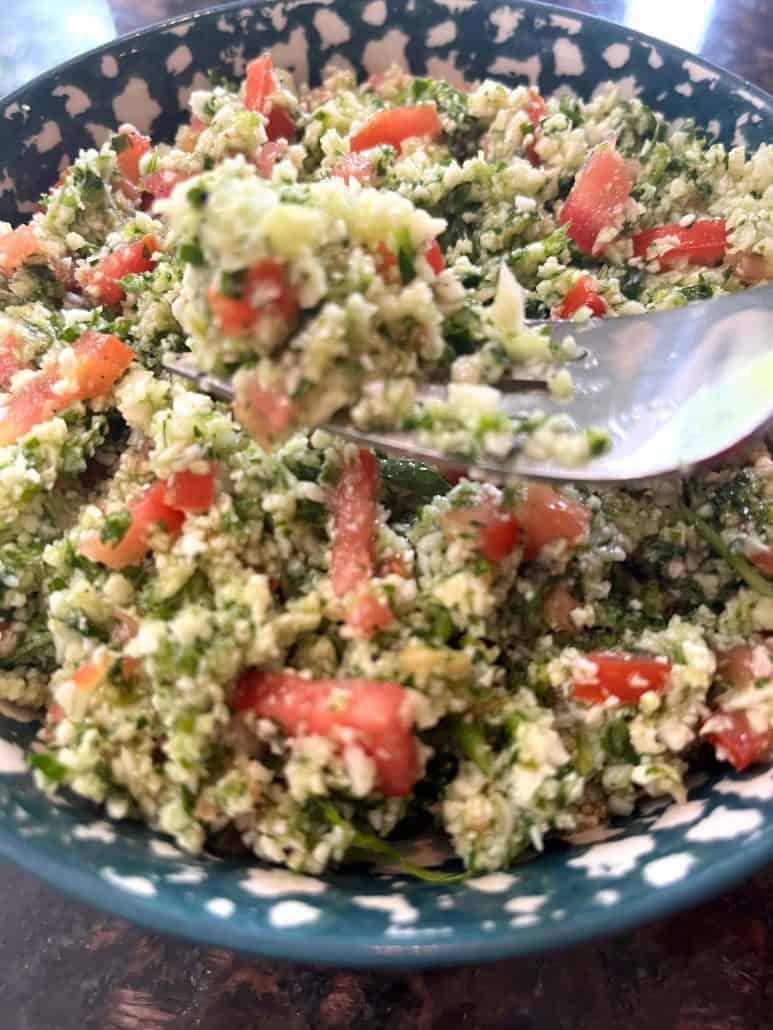A bowl of cauliflower tabbouleh salad filled with finely chopped cauliflower, tomatoes, cucumbers, and parsley, lightly dressed with lemon.
