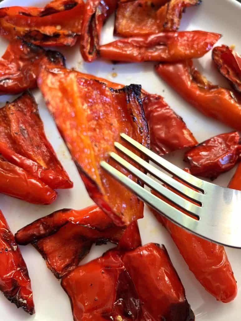 Close-up of a fork lifting, roasted ancient red sweet pepper slice. 