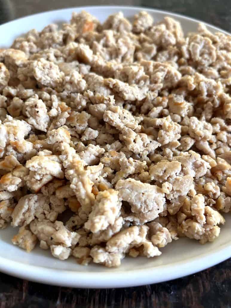 Cooked ground chicken on a plate, showing its juicy and crumbly texture, perfect for adding to various dishes.