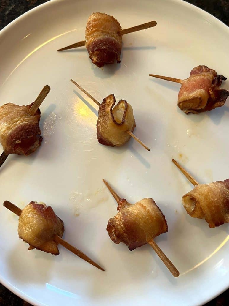 A close-up of crispy bacon-wrapped scallops on a white plate, showcasing their golden-brown texture.