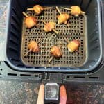 Golden-brown bacon-wrapped scallops freshly cooked in an air fryer basket, showing their crispy texture and perfect doneness.