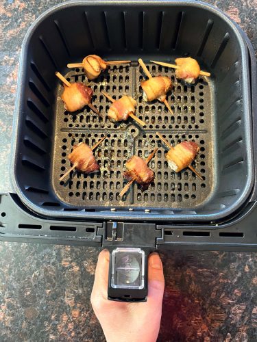 Golden-brown bacon-wrapped scallops freshly cooked in an air fryer basket, showing their crispy texture and perfect doneness.