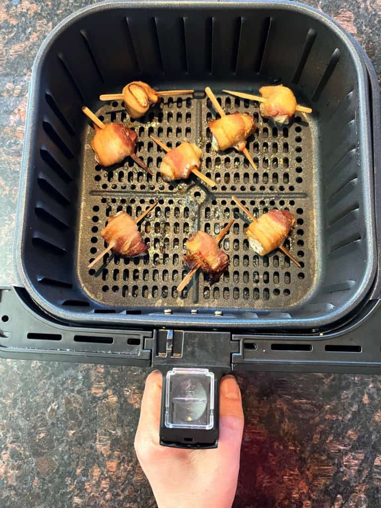 Golden-brown bacon-wrapped scallops freshly cooked in an air fryer basket, showing their crispy texture and perfect doneness.