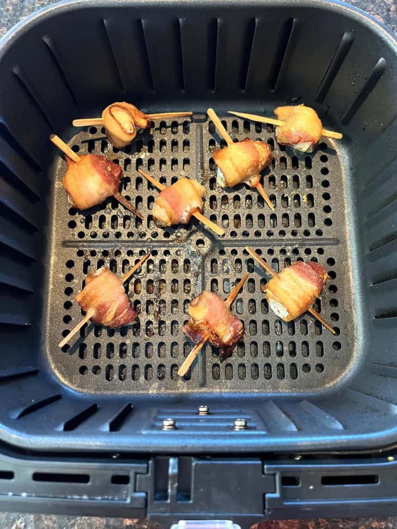 Golden-brown bacon-wrapped scallops in an air fryer basket, evenly cooked and ready to enjoy as a crispy, savory appetizer.