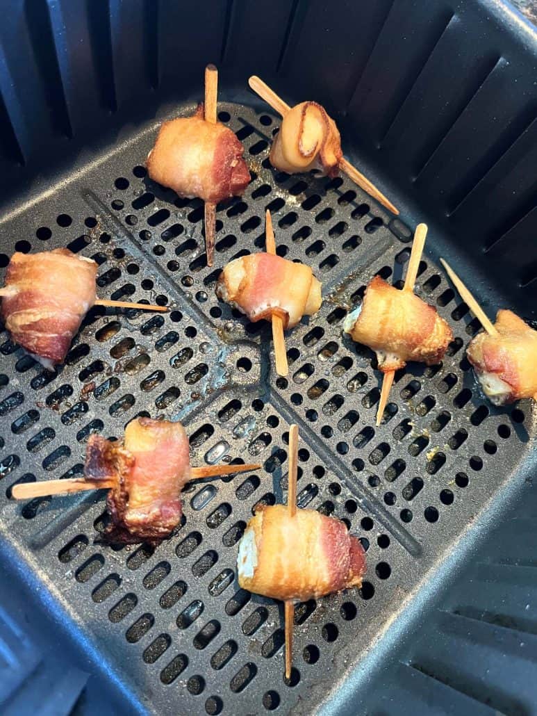 Crispy bacon-wrapped scallops in an air fryer basket, cooked to perfection and ready to serve.