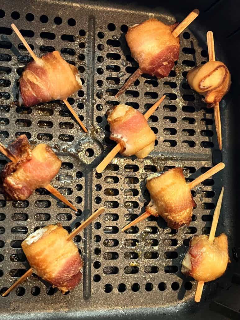 Close-up of crispy bacon-wrapped scallops in an air fryer basket, showcasing their golden-brown texture and perfectly cooked bacon.