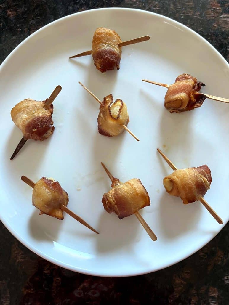 A white plate with crispy bacon-wrapped scallops on skewers, freshly cooked and ready to serve as a delicious appetizer.